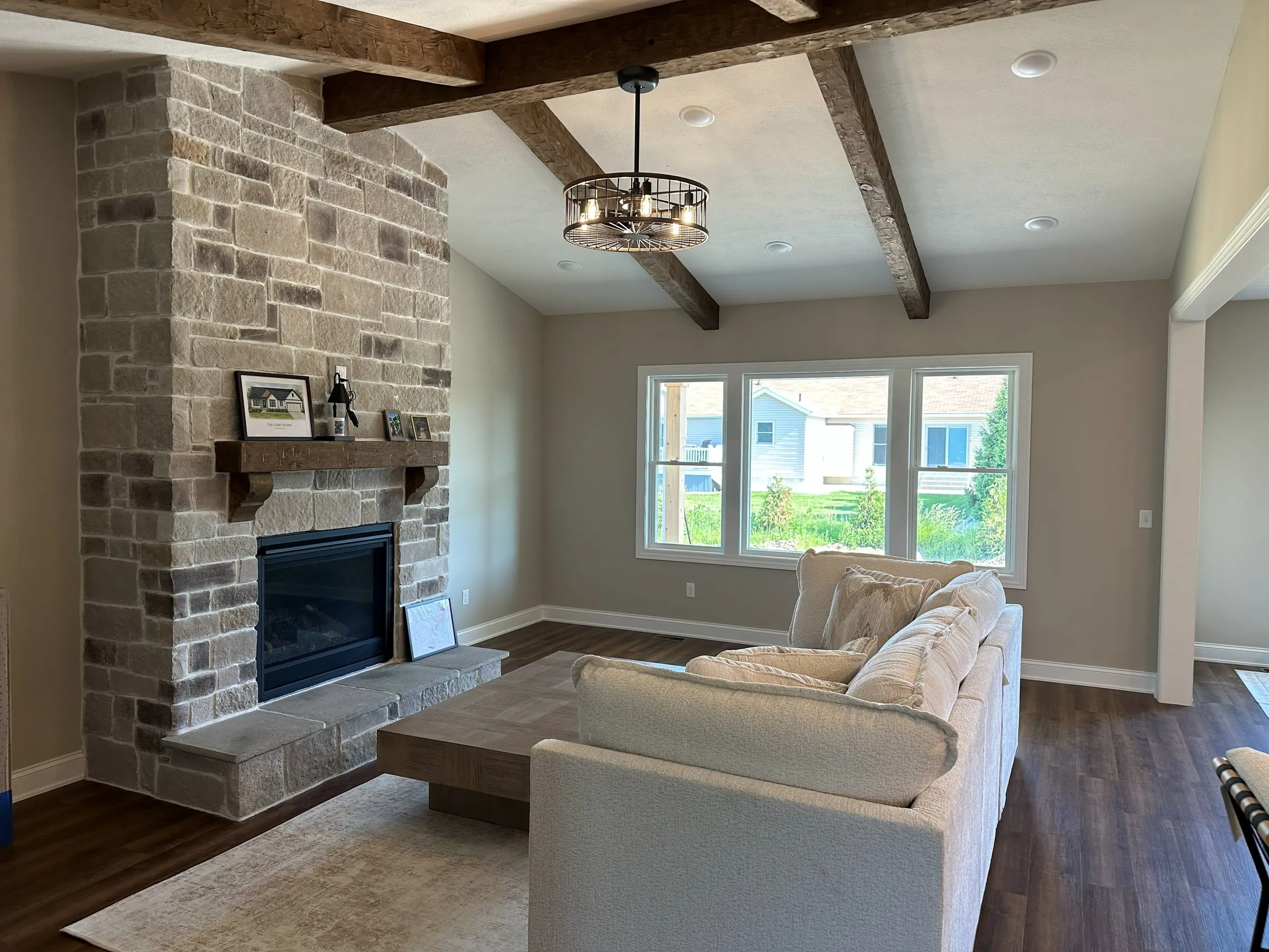 Model home great room with a stone fireplace and exposed wood beams