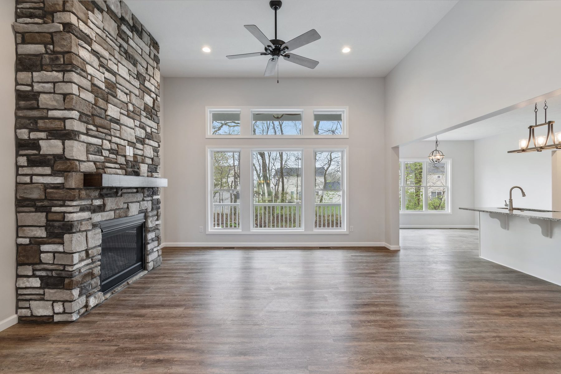 Great room with a stone fireplace, vaulted ceiling, and tall windows